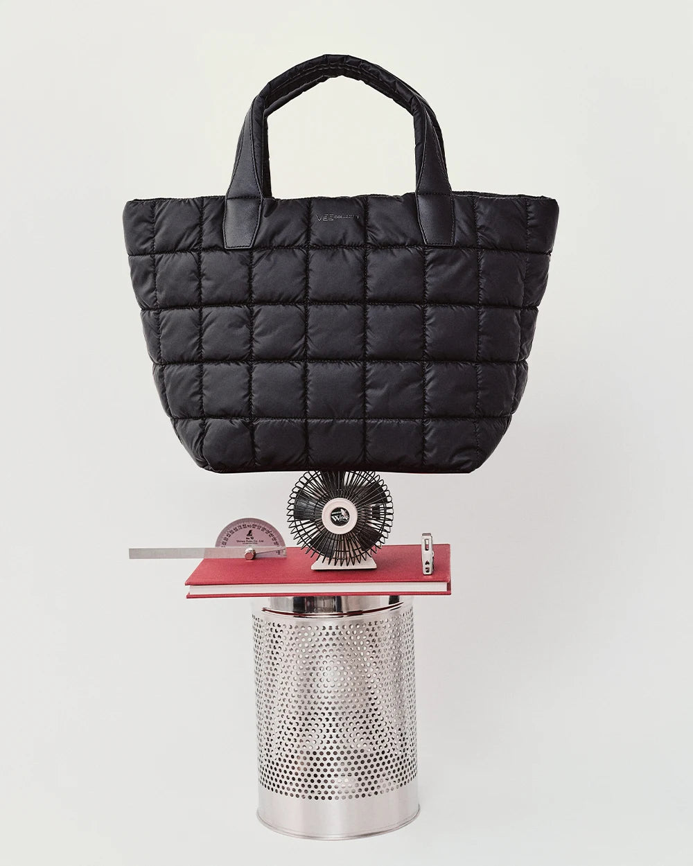 Porter Tote Bag Medium in black by Vee Collective displayed balancing on a sculptural arrangement of metal and red geometric objects.