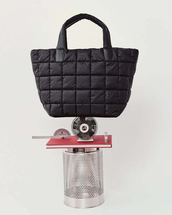 Porter Tote Bag Medium in black by Vee Collective displayed balancing on a sculptural arrangement of metal and red geometric objects.