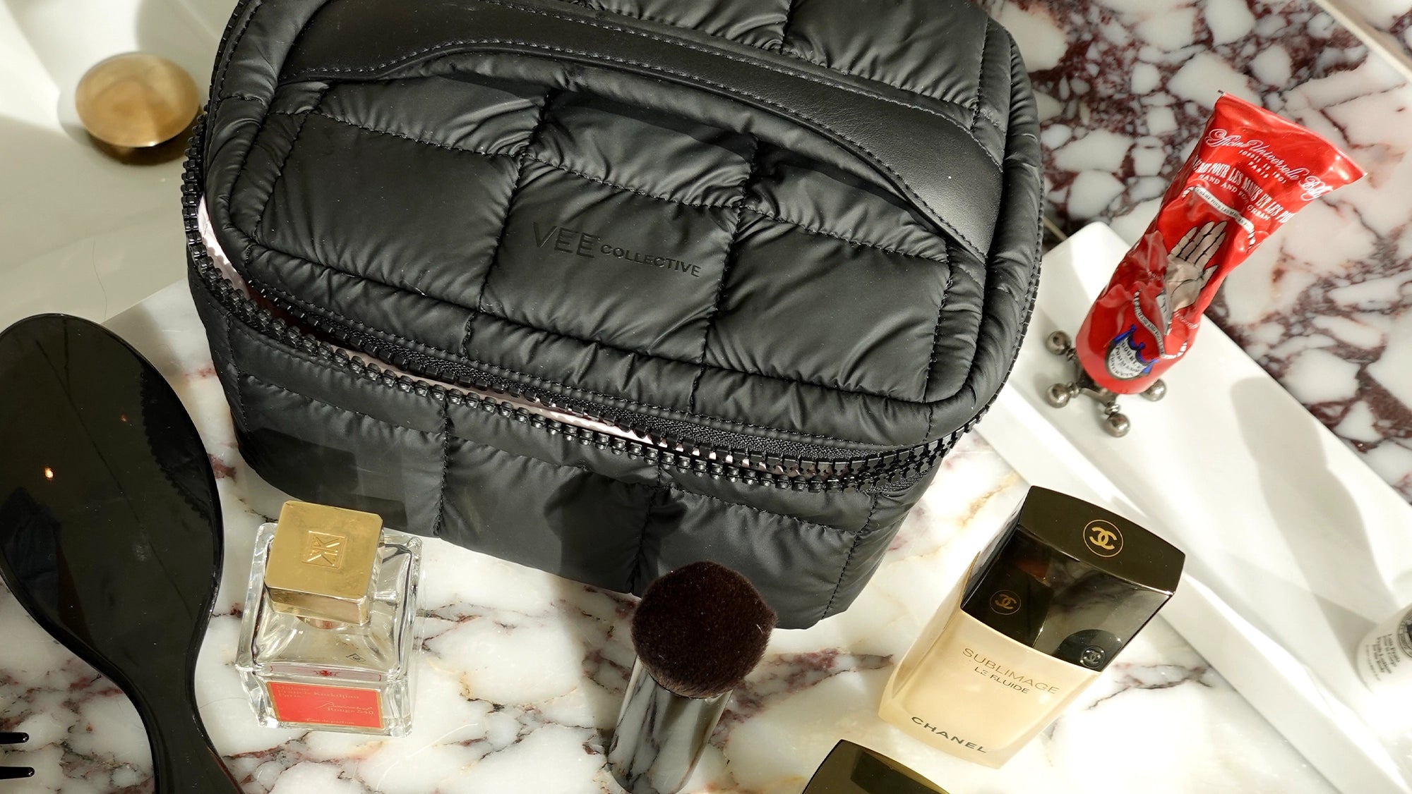 Black quilted cosmetic Vanity Case on a marble surface with makeup items around
