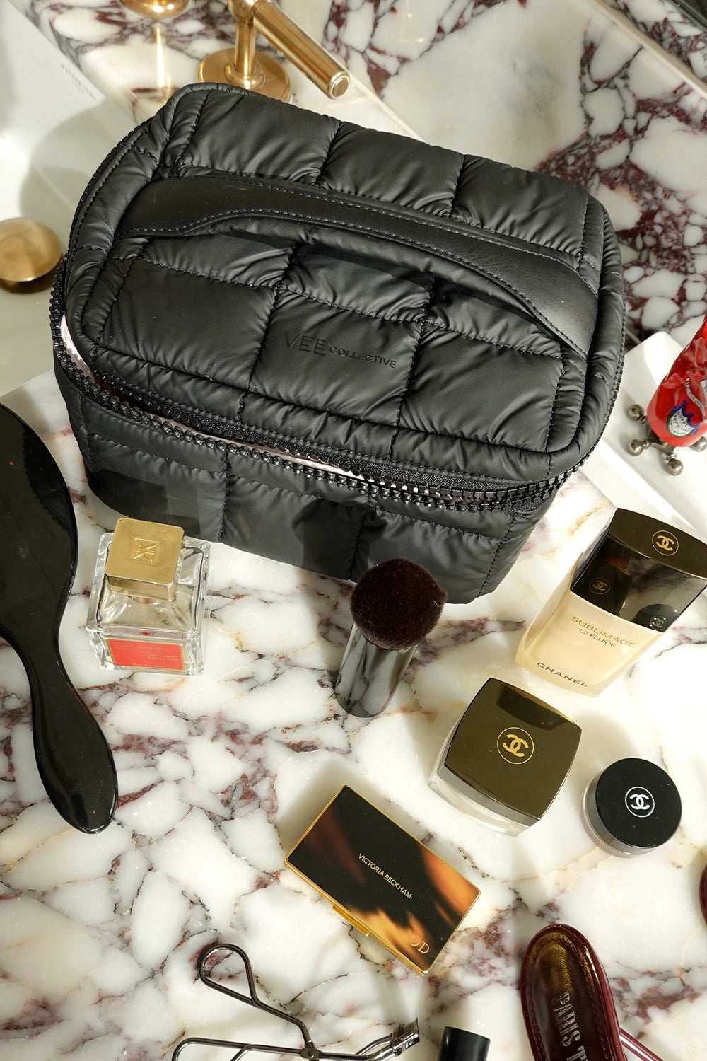Black quilted makeup Vanity Case with various cosmetic items on a marble surface