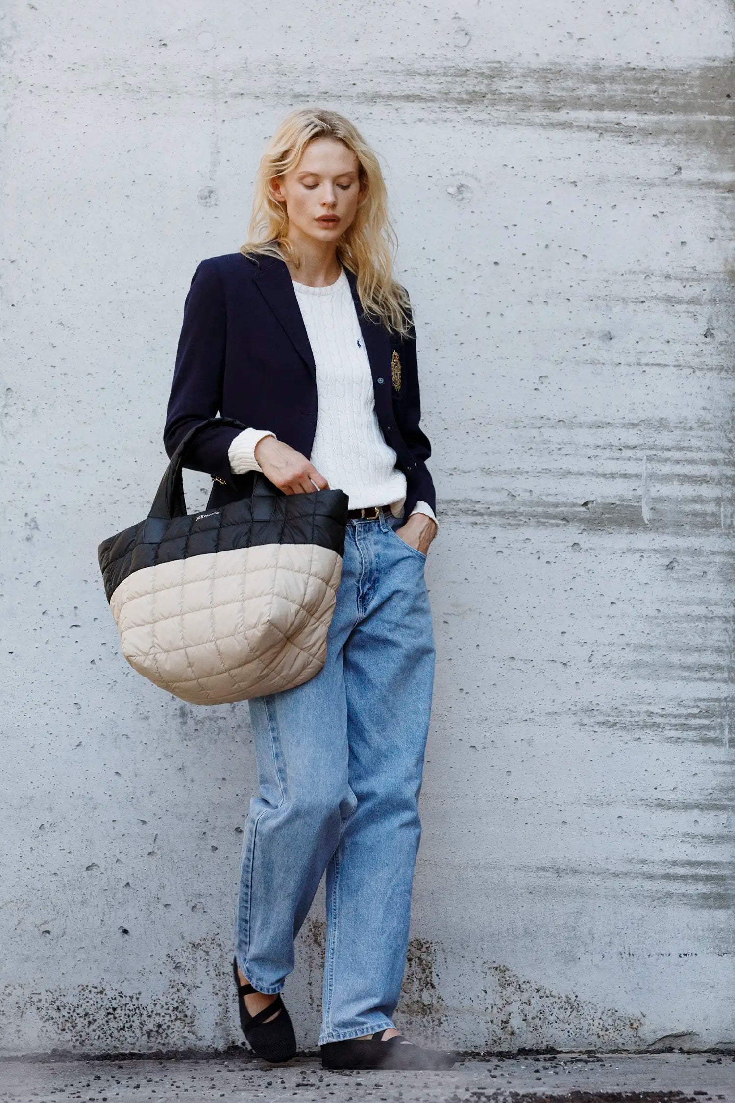 Woman holding a quilted black-beige handbag against a textured wall