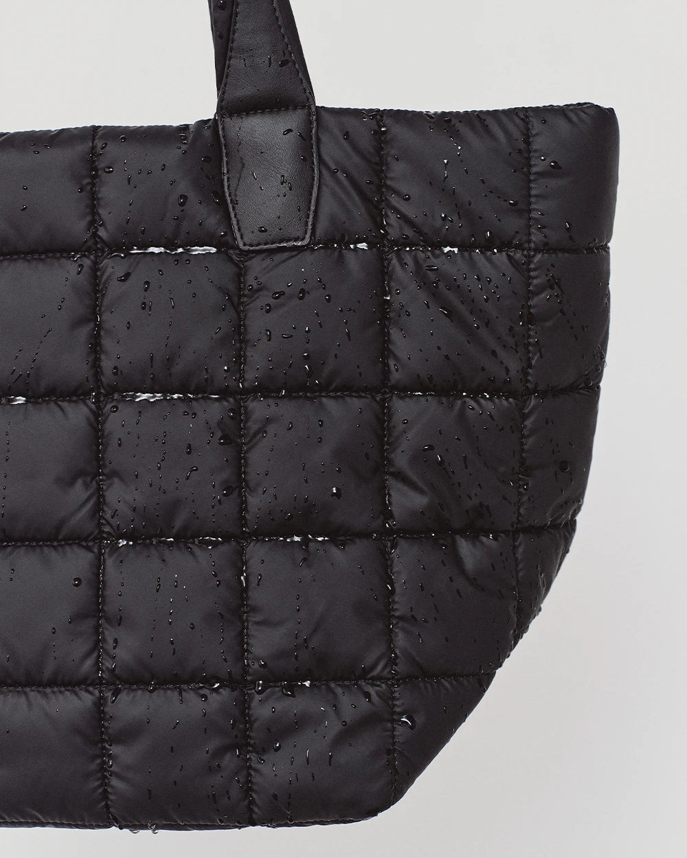 Black Porter Medium Tote Bag by Vee Collective with a quilted finish shown with water droplets on the surface, highlighting its water-resistant material and modern, durable design.