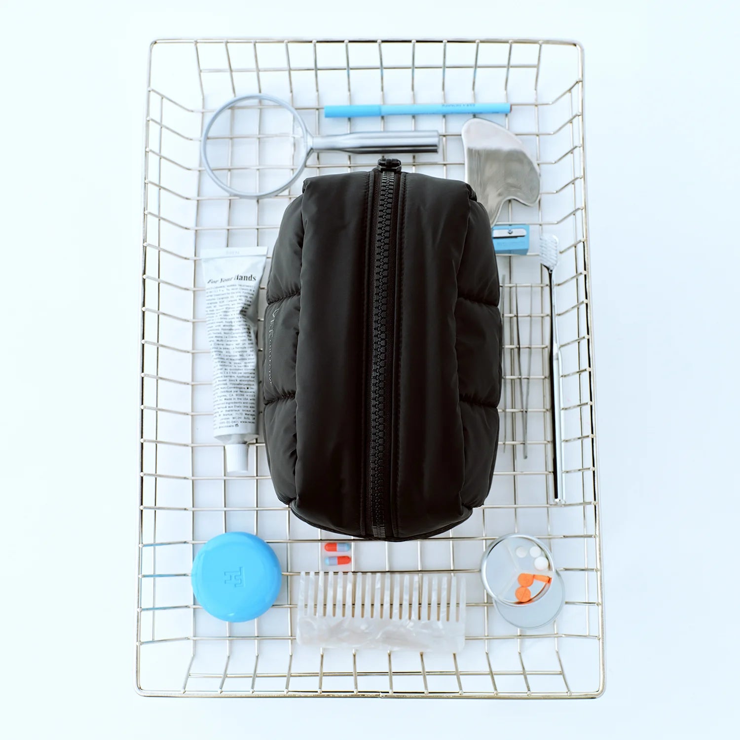 Top-down view of a basket containing the Porter Cosmetics Pouch Medium by Vee Collective along with several cosmetic items, including a comb, cream, magnifying glass, gua sha, toothbrush, and mirror.