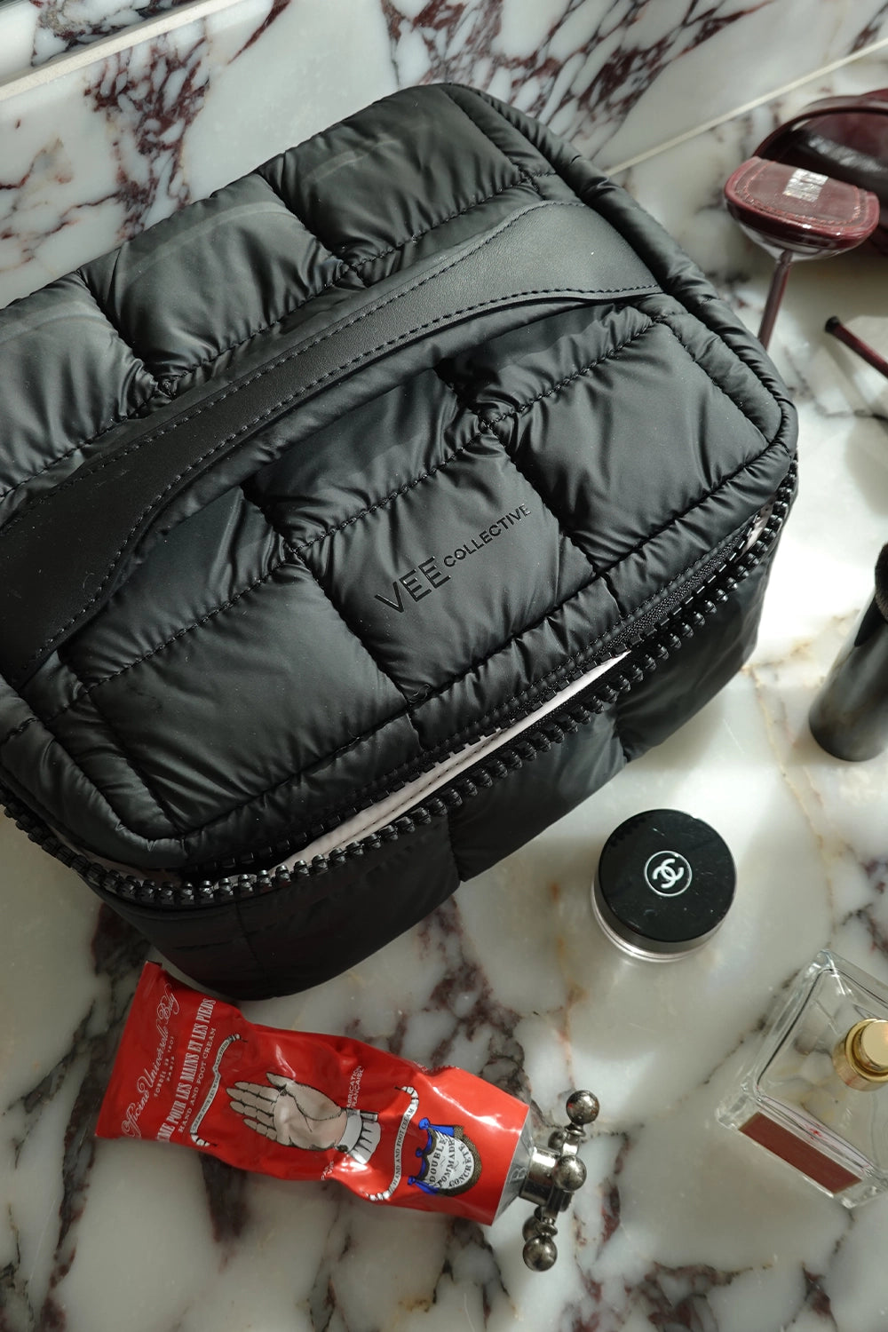 Black quilted Vanity Case on a marble surface with various items around
