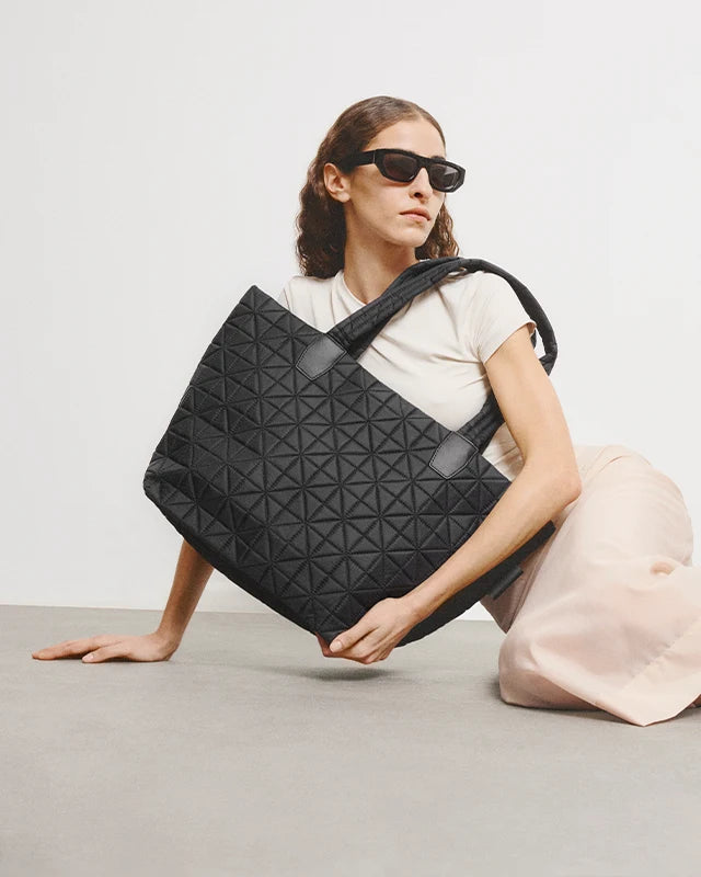 Woman in a beige outfit holding the Vee Medium Tote Bag in Black by Vee Collective in front of her body.