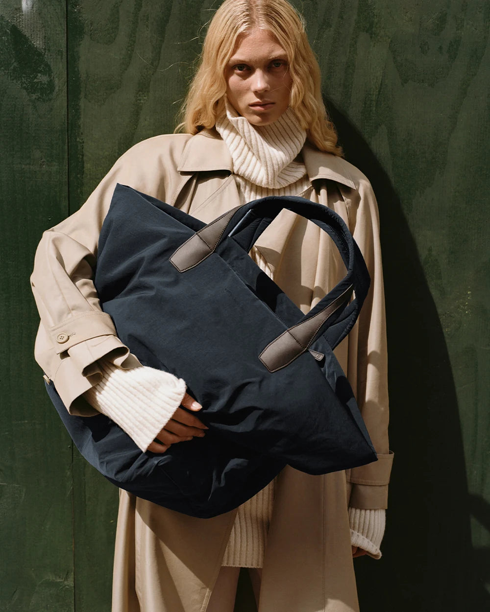 Woman in a beige trench coat holding the Porter Essence Weekender Tote Bag in Midnight Trench by Vee Collective in front of her upper body.