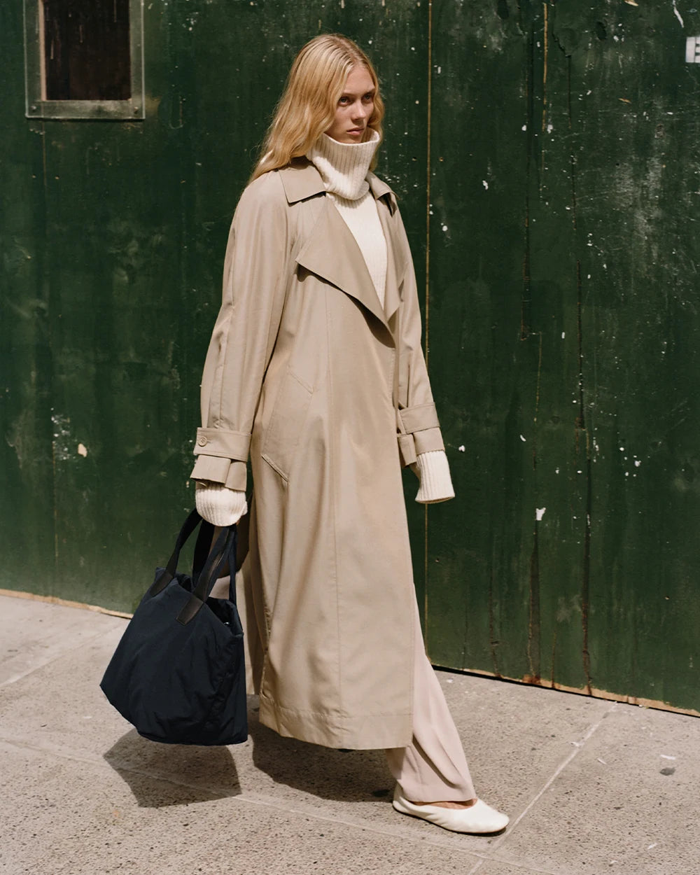 Woman in a beige trench coat holding the Porter Essence Medium Tote Bag in Midnight Trench by Vee Collective in front of her upper body.