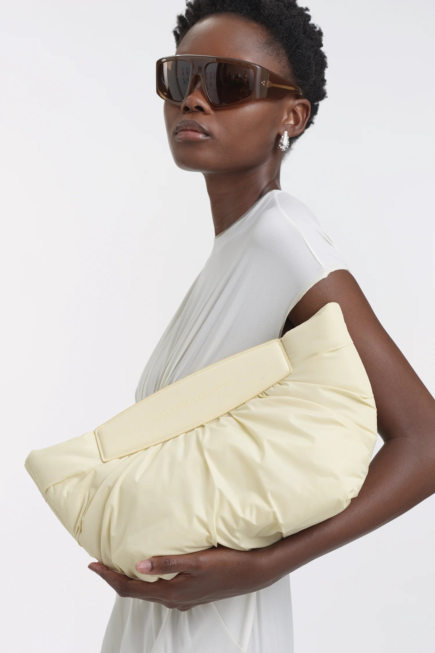 Woman in a white dress holding the Ganvan x Vee Collective Caba Clutch in Buttermilk in her hand.