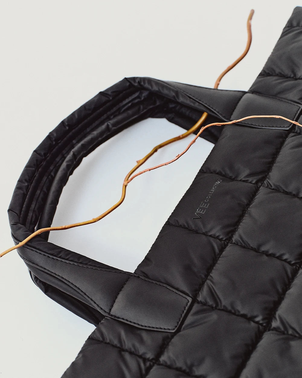 Porter Medium Tote Bag in black by Vee Collective with a wooden stick threaded through the handle cutouts, showcasing the bag’s structured design and distinctive handle construction.