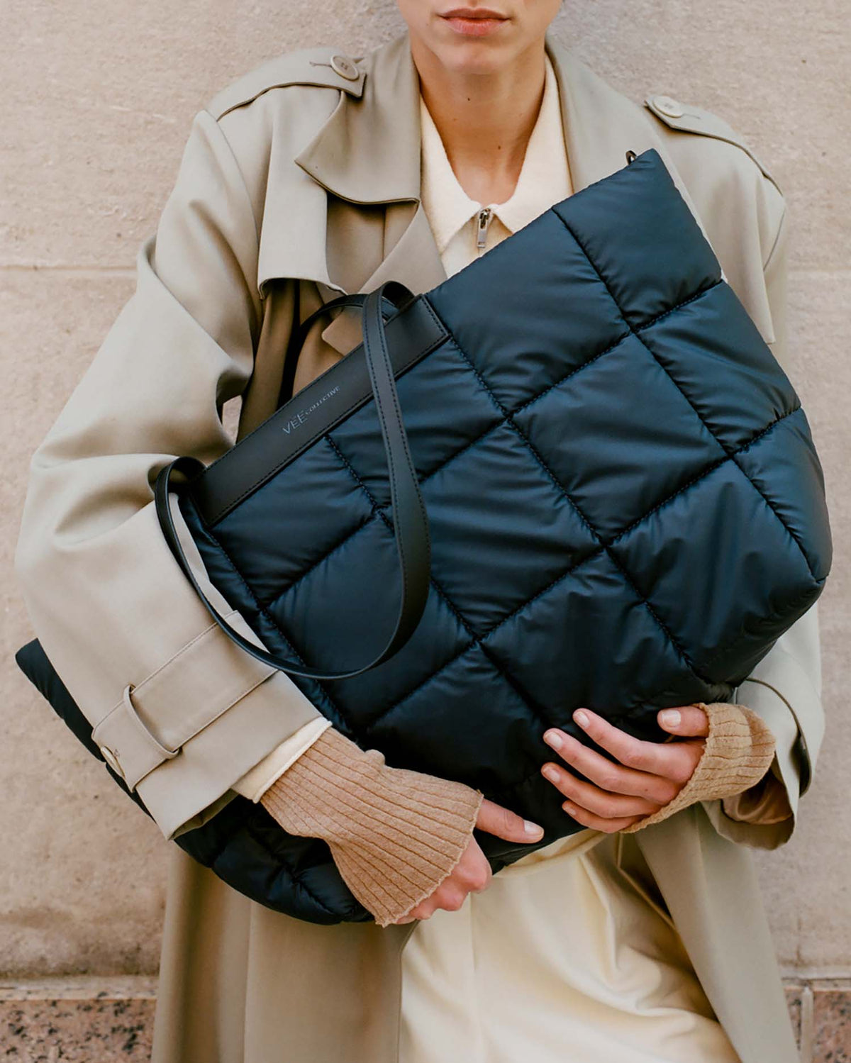 A model wearing a beige trench coat and cream shirt holds a large navy blue Porter Tote bag with black trim and handles.