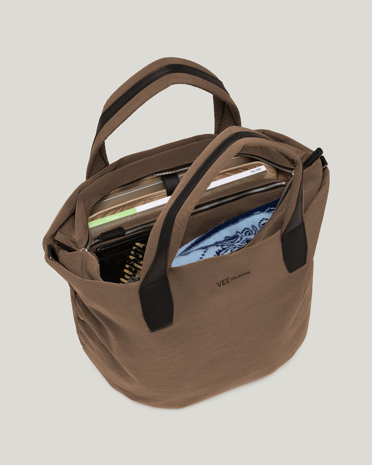 The Essence Trench Medium Mink  bag with black trim and handles, shown open with books and a blue patterned item inside, on white background.