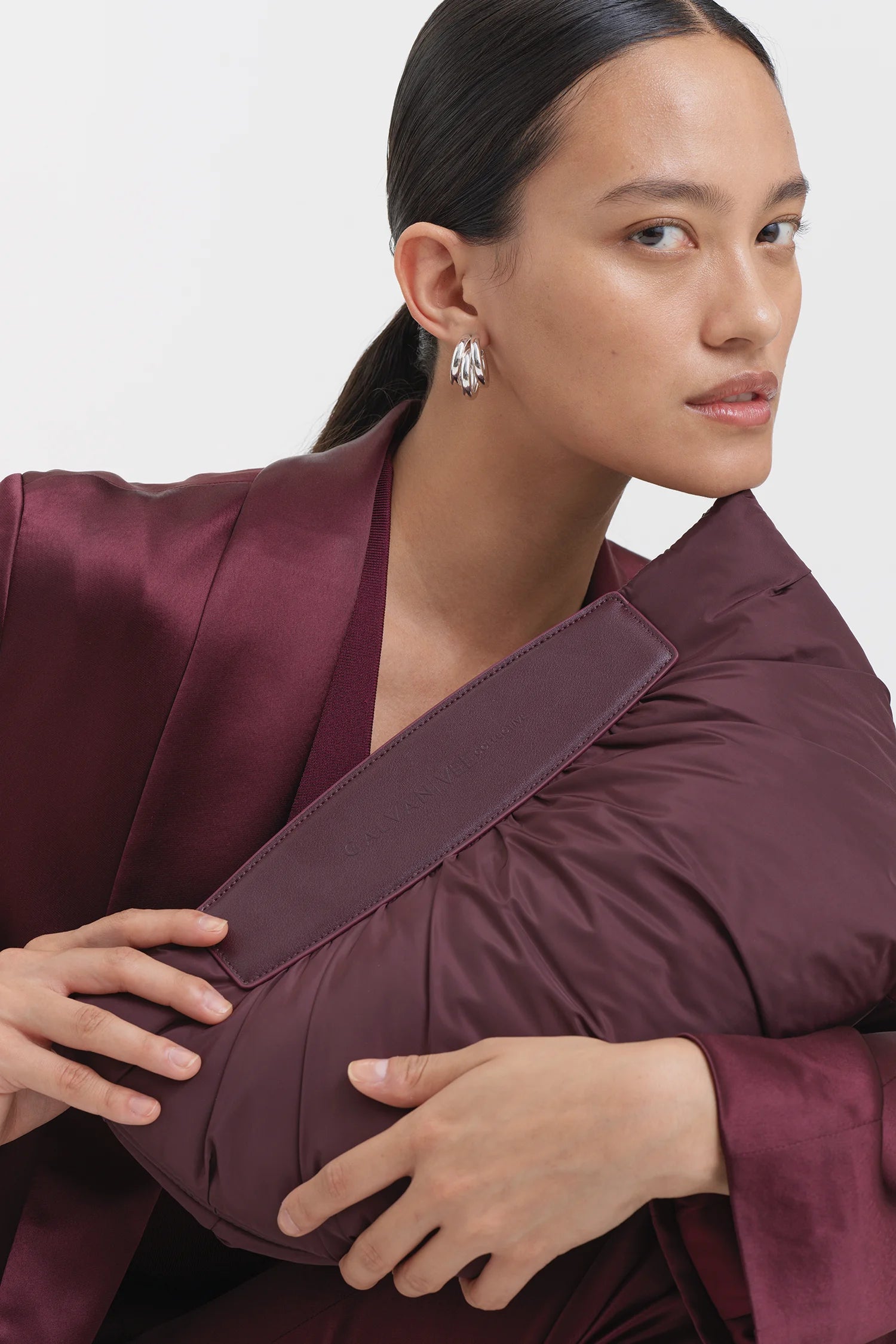 Woman wearing a full mahogany outfit, holding the Galvan x Vee Collective Caba Clutch Bag in mahogany at an angle in front of her upper body, positioned near the chin.