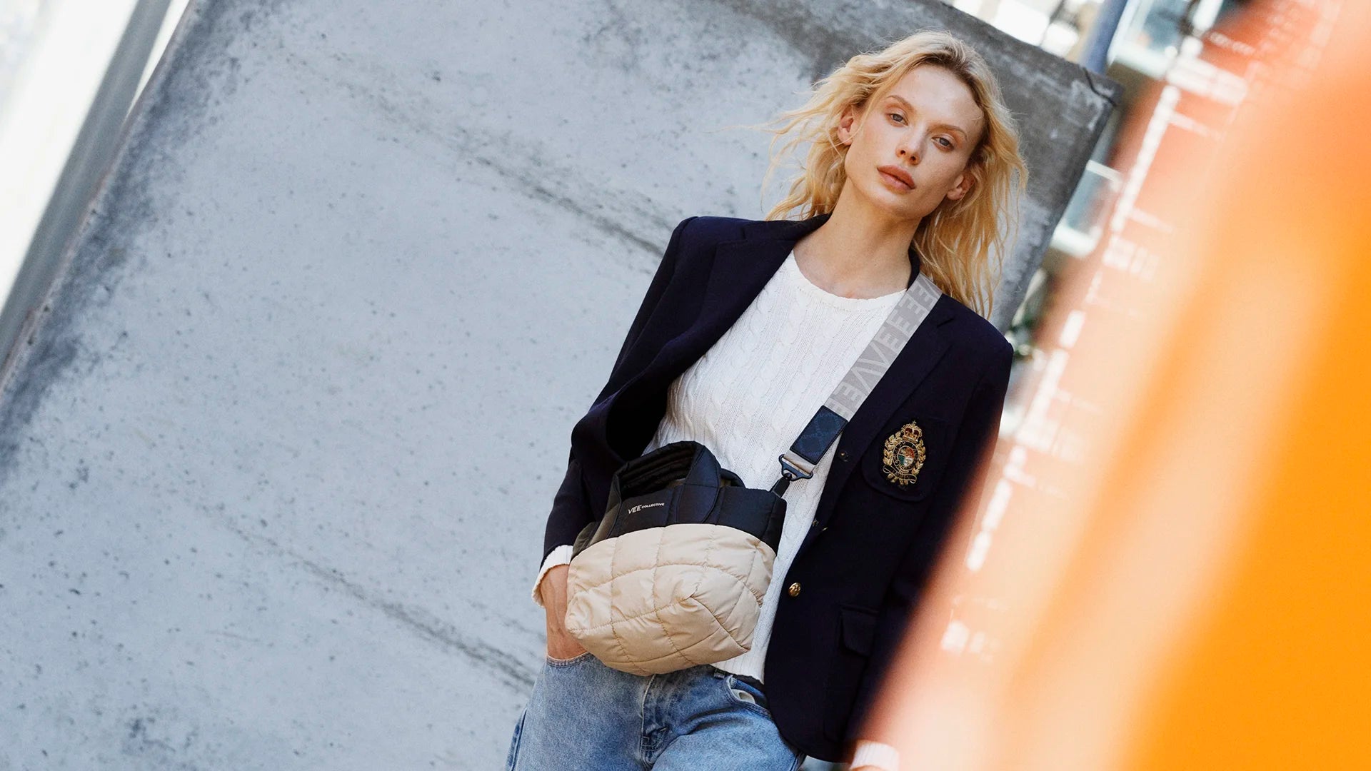 Woman in a stylish outfit with a blazer and jeans, holding a black-beige handbag on a city street.