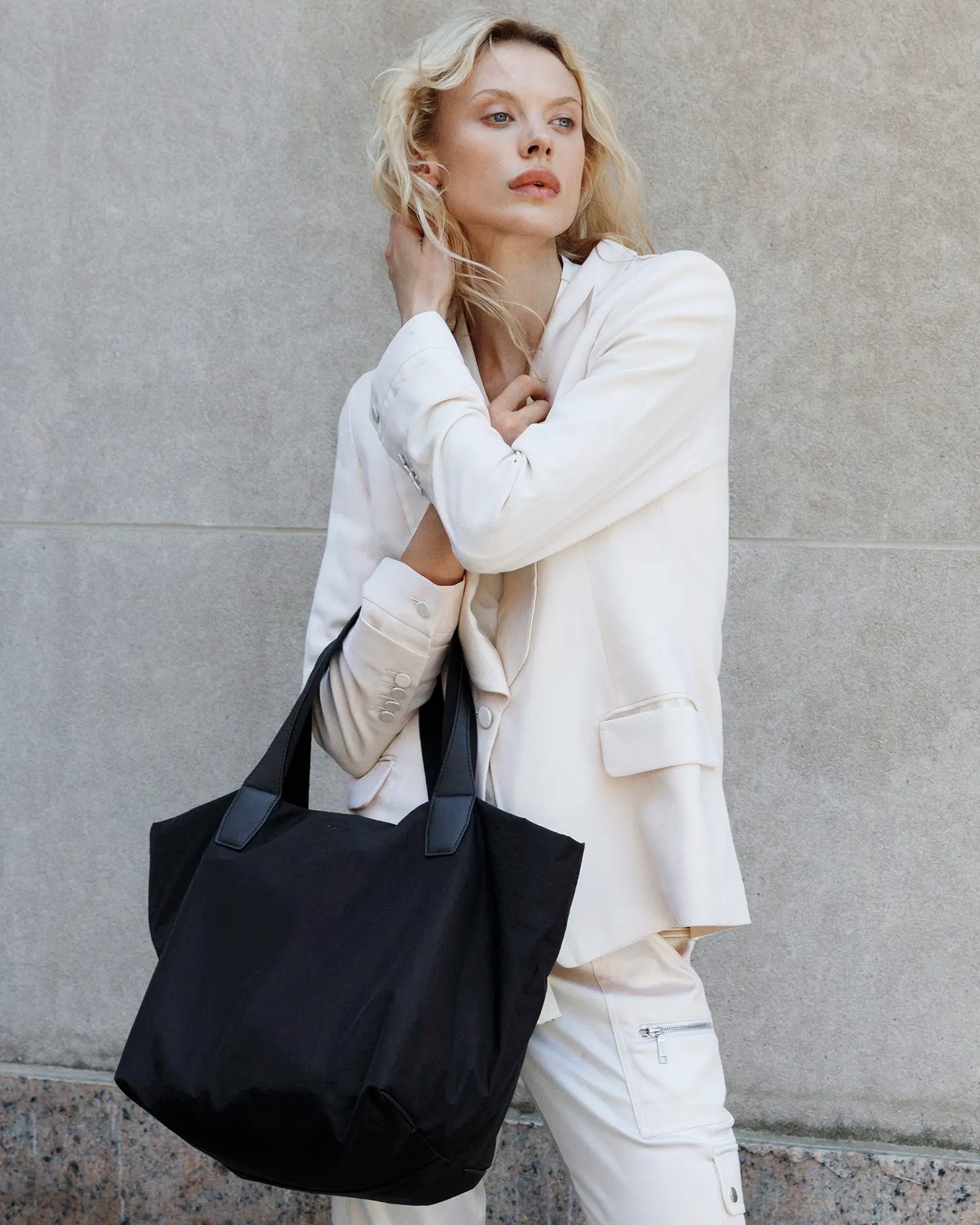Woman holding Porter Essence Paper Black bag against a gray wall