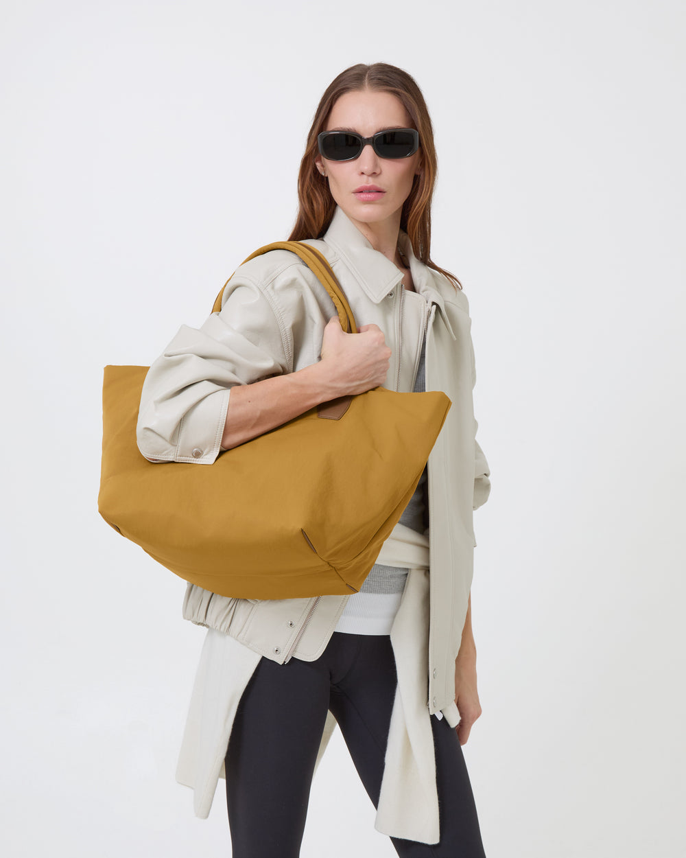 A Modelwearing a light beige trench coat and black sunglasses carries the Essence Medium Tracy Anderson bag over her shoulder, set against a plain white studio background.
Details