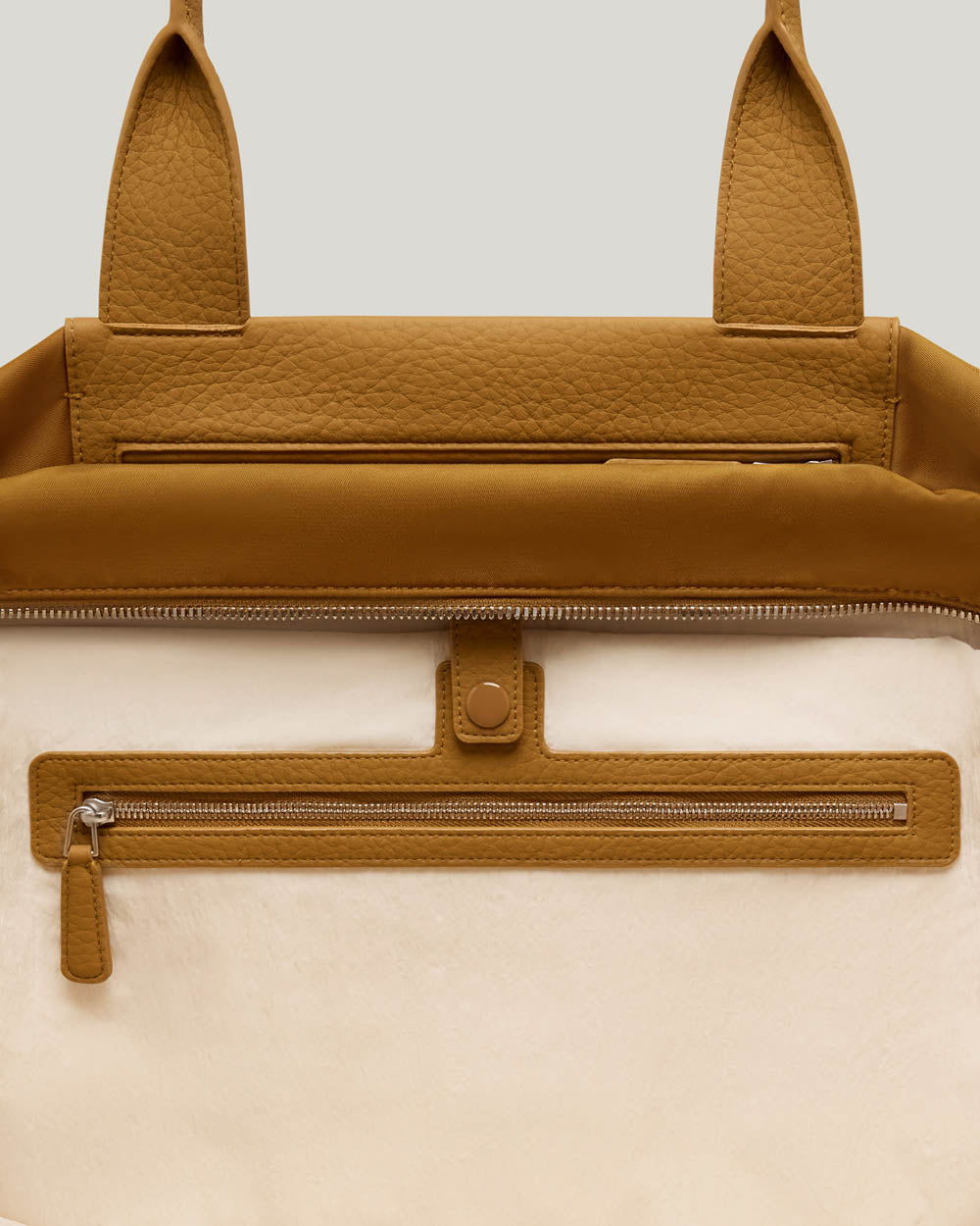 Close-up of the Duo Tote Large Honey Mustard bag. A two-tone design with a warm camel-brown pebbled leather top section and handles, and a cream-colored textured lower body, featuring a horizontal zippered pocket with a matching brown leather frame.