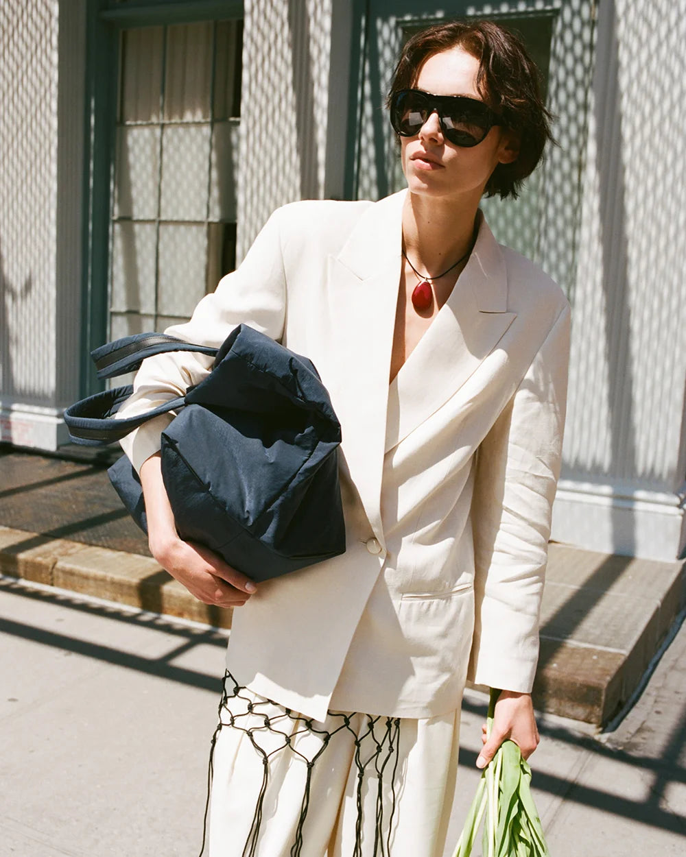 Woman in a white blazer holding a navy bag on a city street.