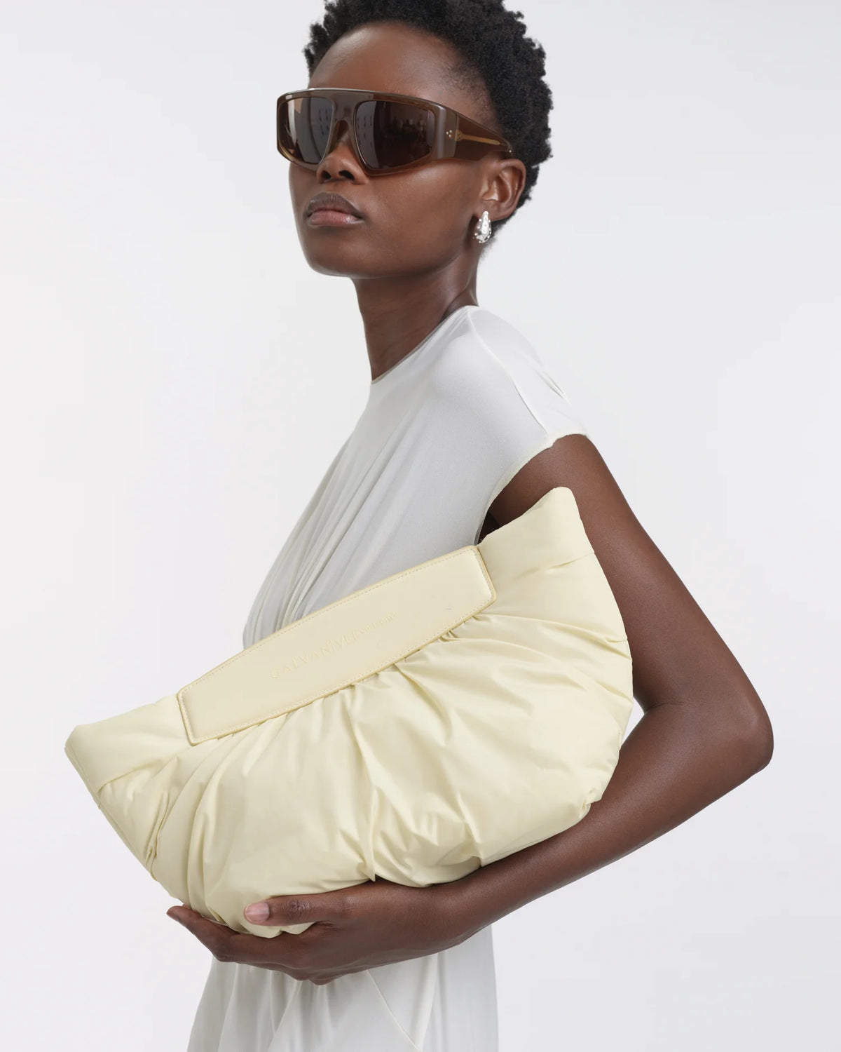Woman holding the Galvan x Vee Collective Caba Clutch Bag in buttermilk resting in her arm.