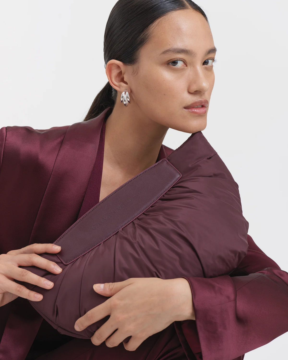 Woman wearing a full mahogany outfit, holding the Galvan x Vee Collective Caba Clutch Bag in mahogany at an angle in front of her upper body, positioned near the chin.