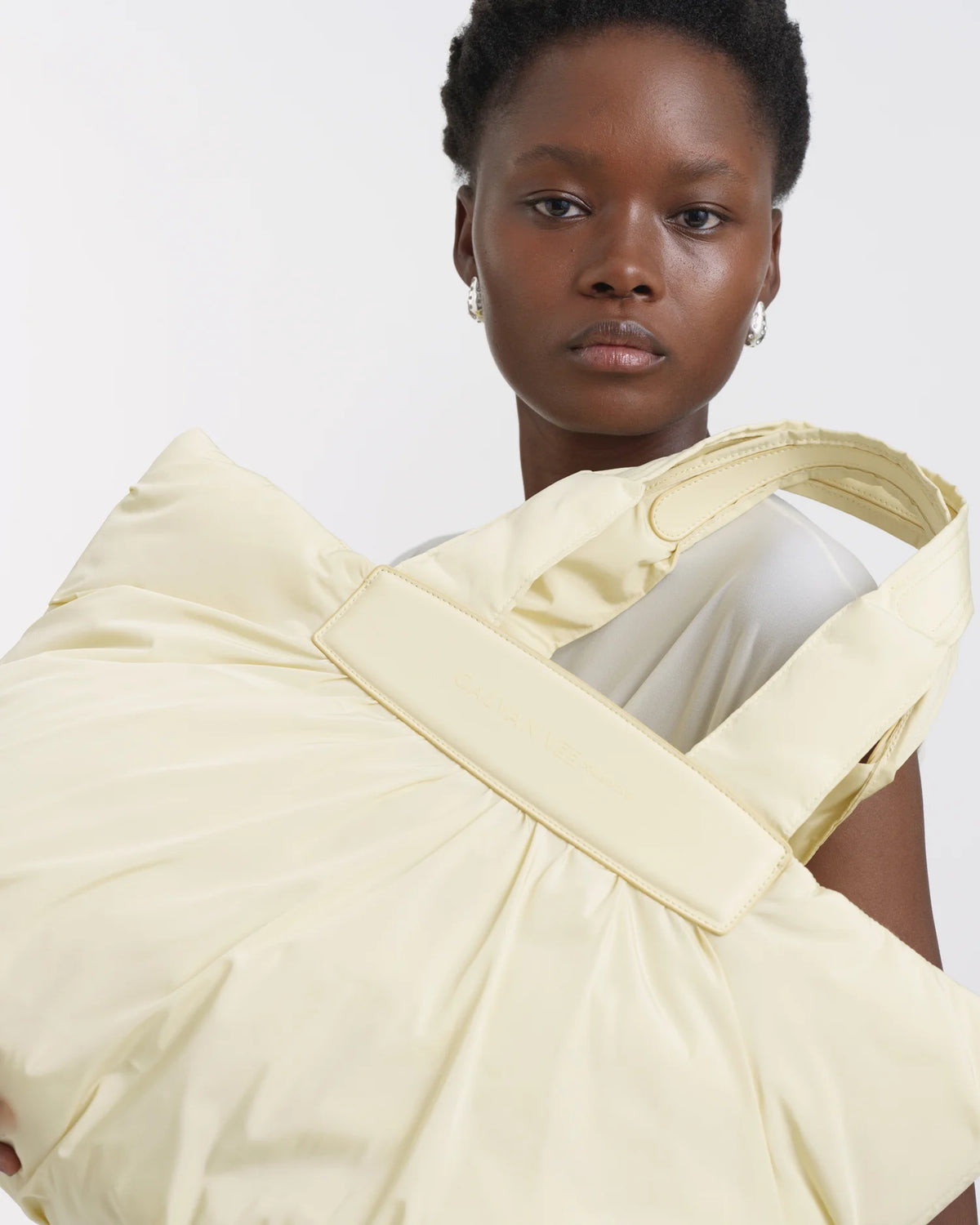 Woman holding the Galvan x Vee Collective Caba Medium Tote Bag in buttermilk in front of her torso, with only her face visible.