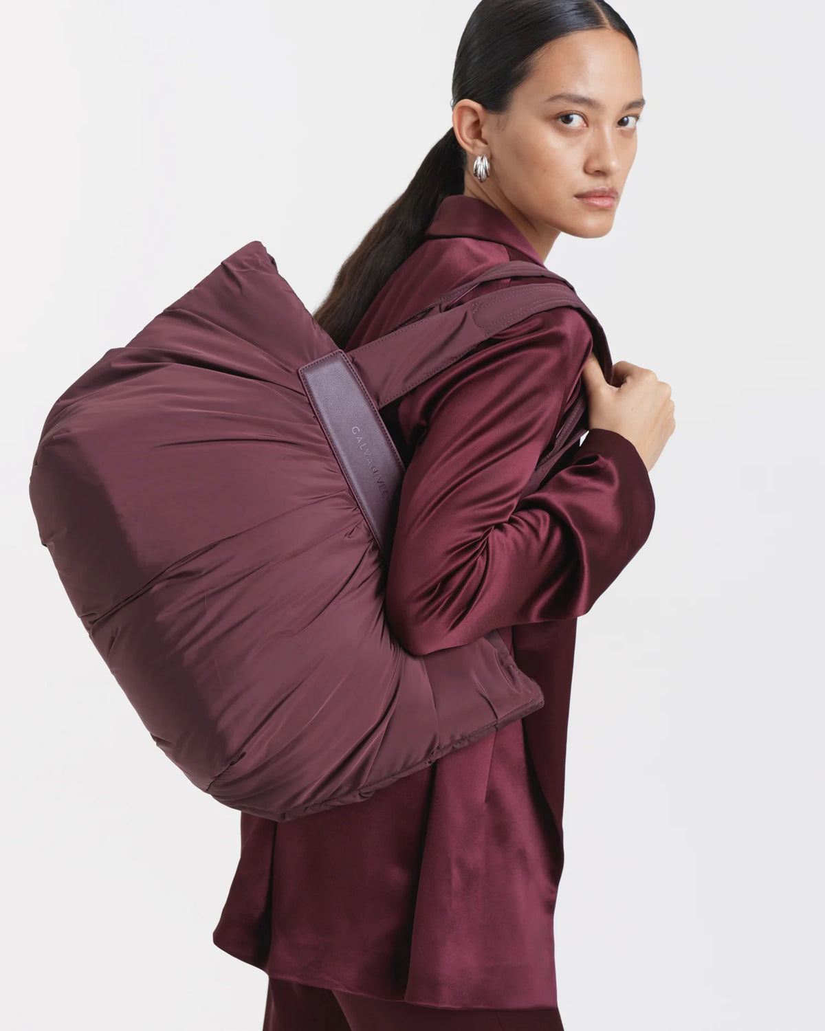 Woman wearing a mahogany outfit carrying the Galvan x Vee Collective Caba Medium Tote Bag in mahogany over her shoulder.
