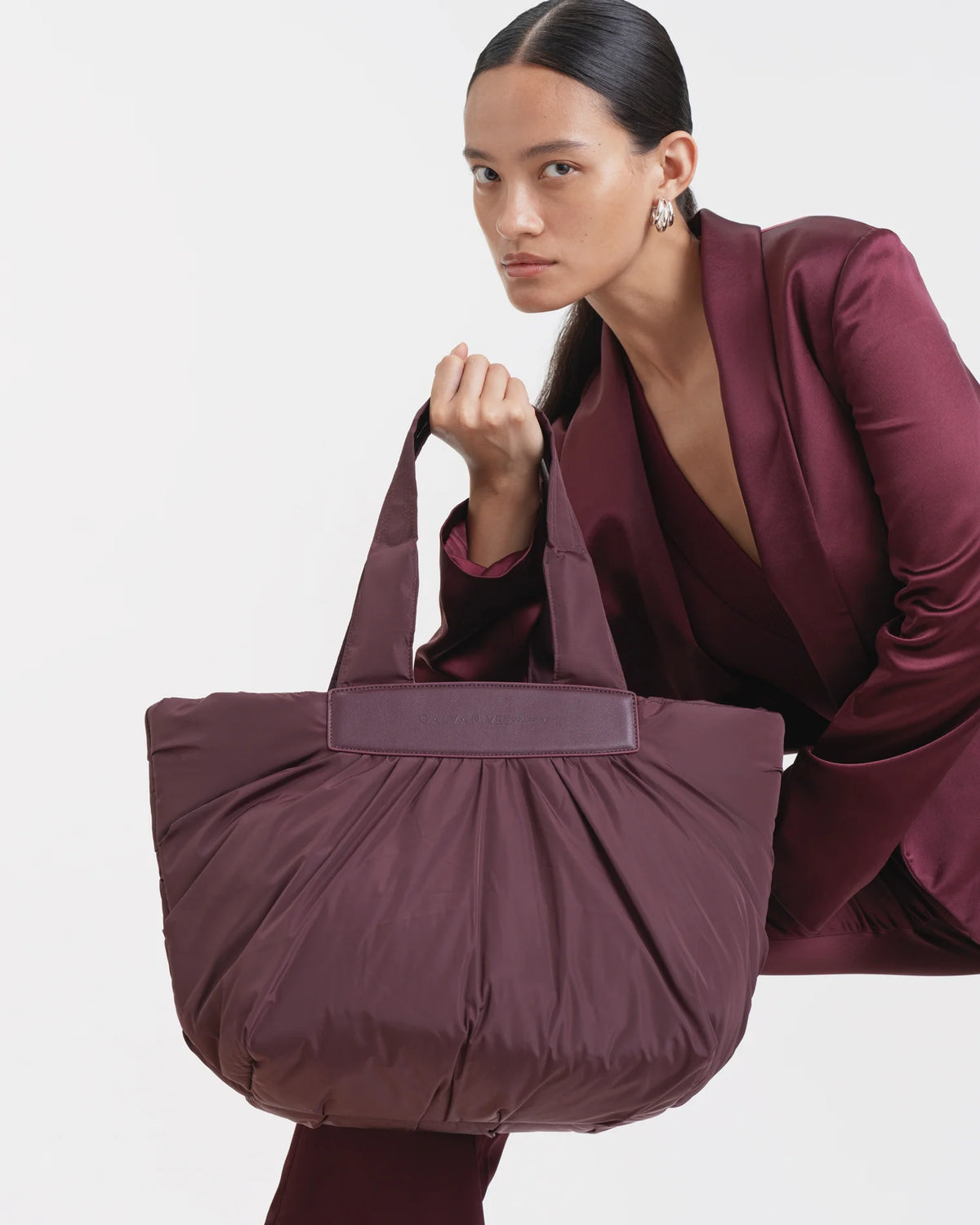 Woman in a matching mahogany outfit holding the Galvan x Vee Collective Caba Medium Tote Bag in mahogany, shown in a three-quarter pose against a clean background.