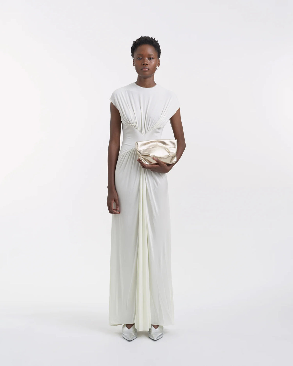 Full-body view of a woman in a white dress holding the Galvan x Vee Collective Evening Clutch Bag in silver metallic in her hand.