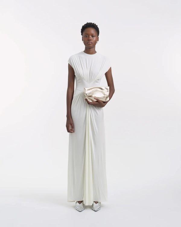 Full-body view of a woman in a white dress holding the Galvan x Vee Collective Evening Clutch Bag in silver metallic in her hand.