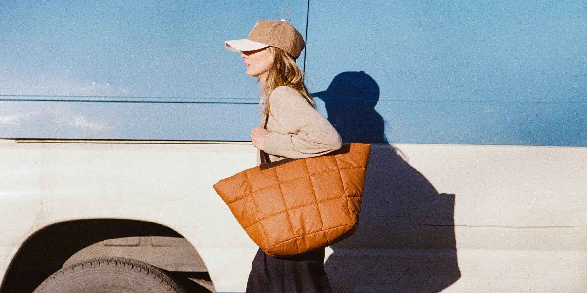 Woman holding  Porter Basque Cognac quilted handbag against a blue white car.