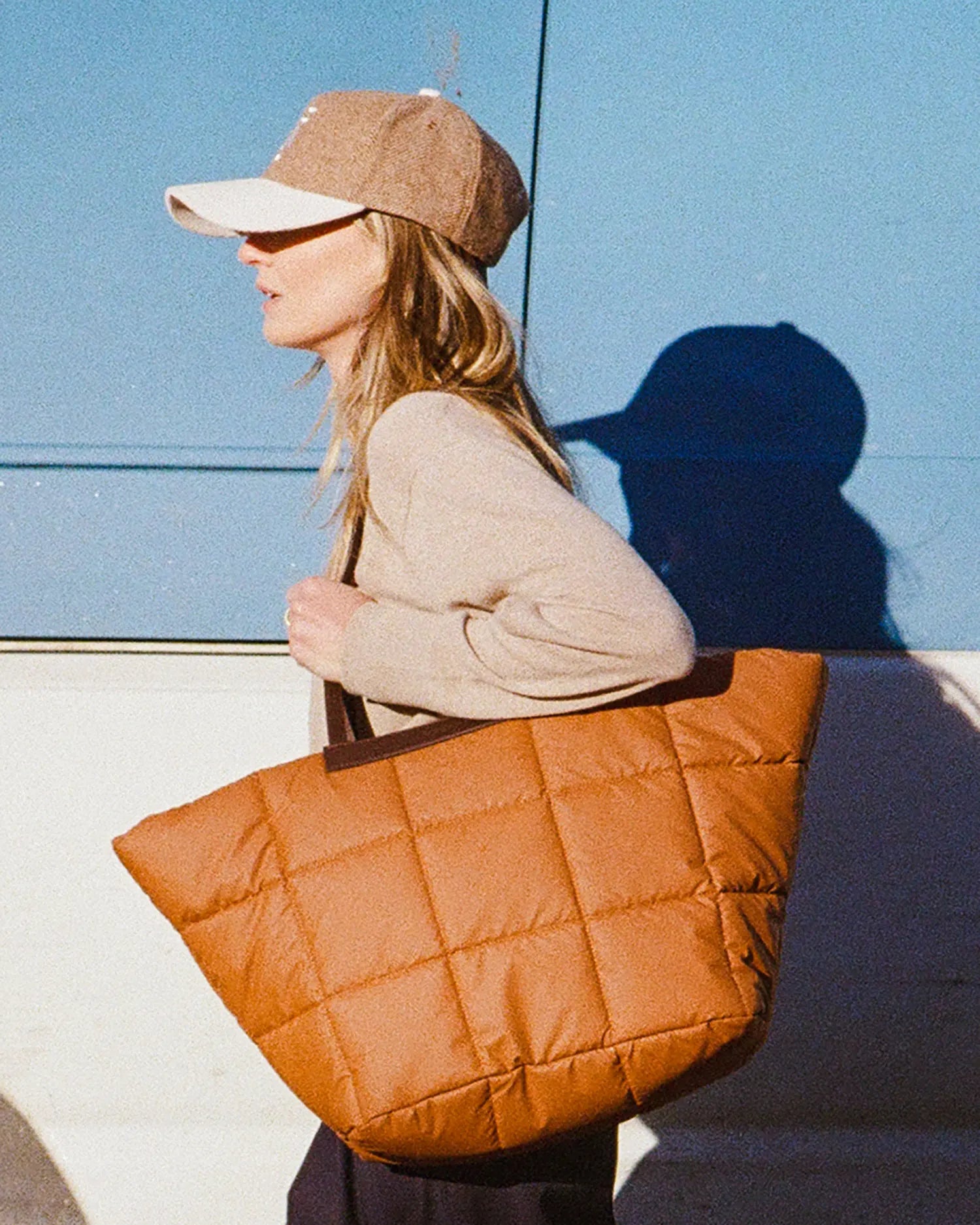 Woman holding  Porter Basque Cognac quilted handbag against a blue white car.