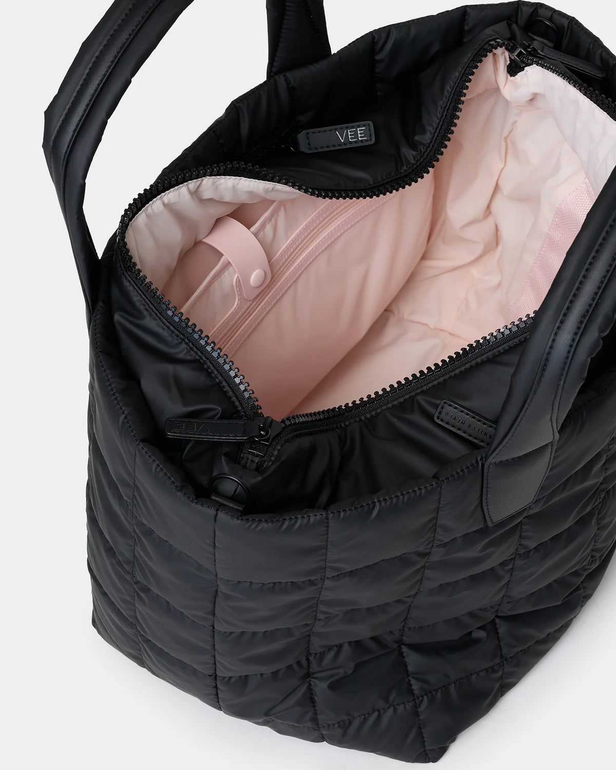 A close-up view of the interior of a black quilted tote bag, featuring a soft pink lining. The bag has a zipper closure and a small inner pocket, showcasing its spacious design for everyday use.