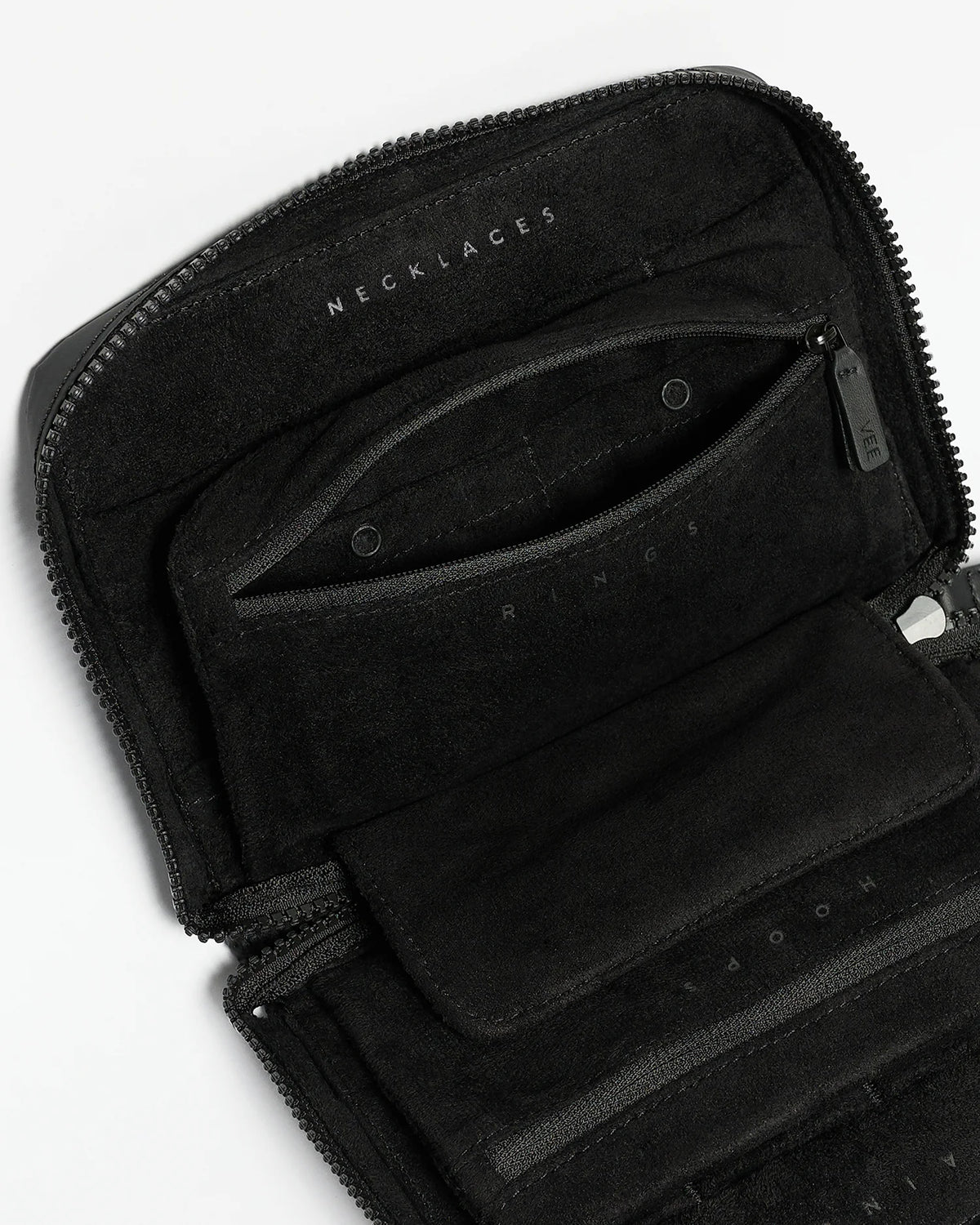 Close-up view of the interior of a black jewelry case featuring a soft lining and multiple zippered compartments labeled for necklaces, rings, and hoops. The sleek design emphasizes organization, ideal for secure travel storage.