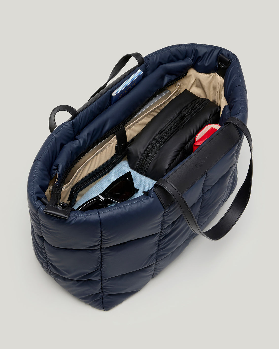 The Porter Marche Large Dark Navy tote bag shown open from an overhead angle, revealing a beige interior organizer, black zippered pocket, sunglasses, and other accessories inside, set against a white background.