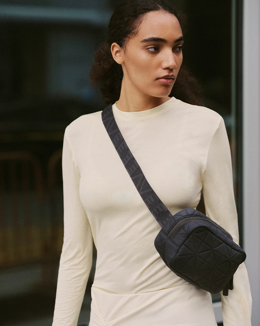 Close-up of a woman wearing a cream long-sleeve top with a black quilted Vee Collective belt bag worn crossbody