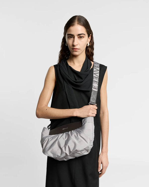 On-body picture of a woman carrying the Caba Clutch bag in Dove crossbody by Vee Collective, wearing a minimalistic outfit against a clean studio background.