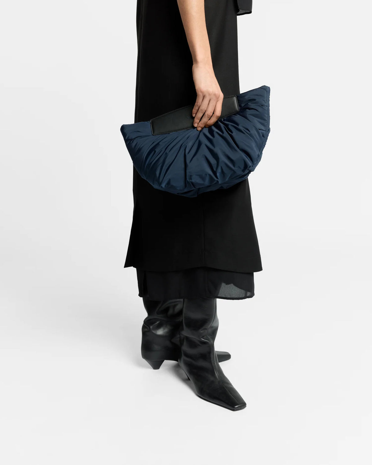 Half-body close-up of a woman carrying the Caba Clutch bag in Marine by Vee Collective, wearing a minimalistic outfit against a clean studio background.