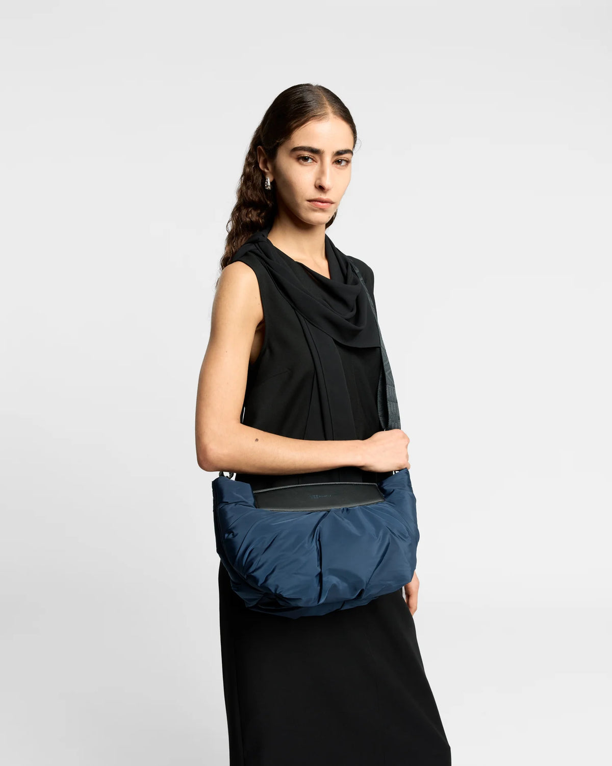 On-body picture of a woman carrying the Caba Clutch bag in Marine by Vee Collective, wearing a minimalistic outfit against a clean studio background.