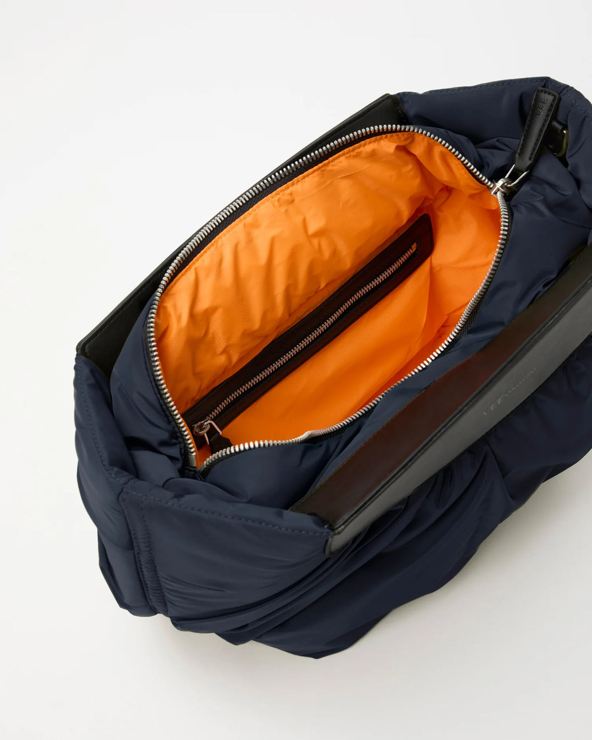 Open Vee Collective Caba Clutch in Marine, showing the quilted exterior, top zipper, and orange interior of the Clutch bag.