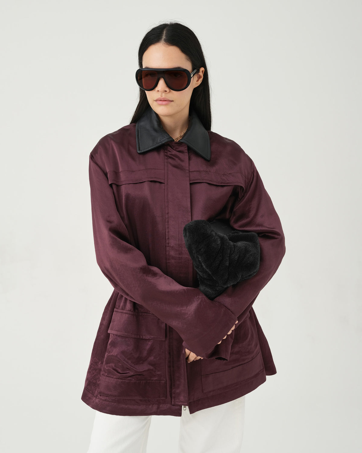 A close-up fashion photo of a model wearing a dark burgundy jacket and holding a black Caba Fur Clutch bag in their hand.