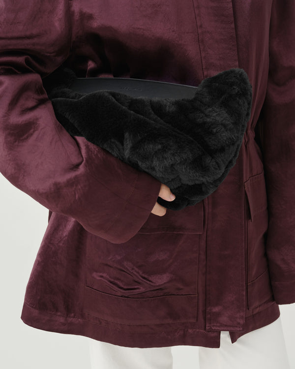 A close-up fashion photo of a model wearing a dark burgundy jacket and holding a black Caba Fur Clutch bag in their hand.