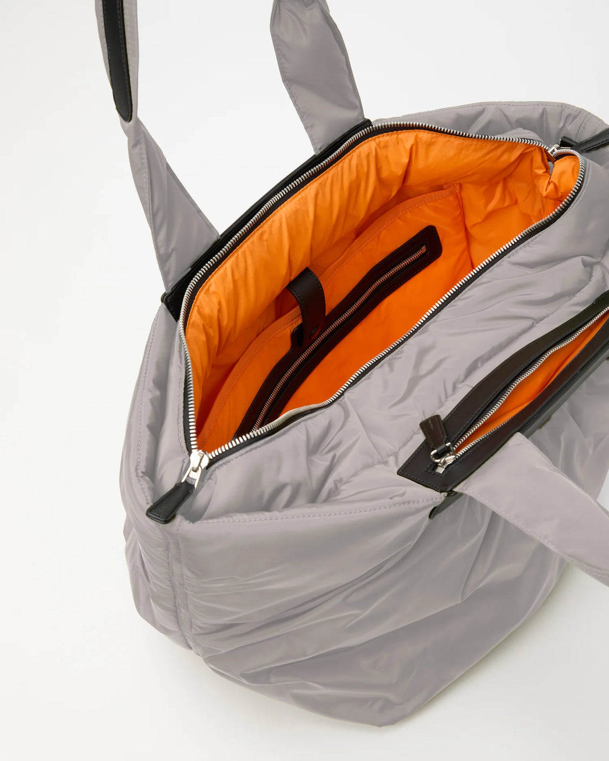 Open Vee Collective Caba Tote Bag Medium in Dove, showing the quilted exterior, top zipper, and orange interior of the tote bag.