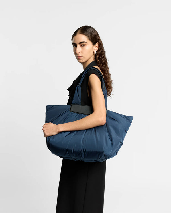 On-body picture of a woman carrying the Caba Tote bag Mediumi in Marine by Vee Collective, wearing a minimalistic outfit against a clean studio background.