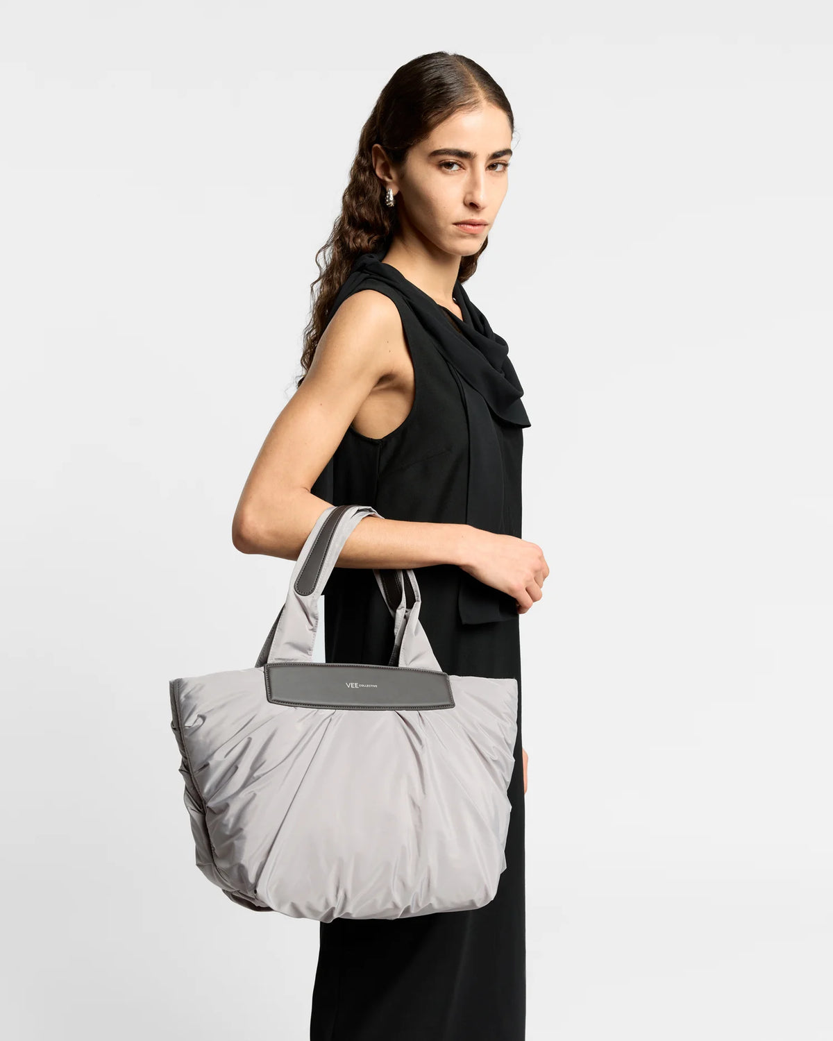 On-body picture of a woman carrying the Small Caba Tote Bag in Dove by Vee Collective, wearing a minimalistic outfit against a clean studio background.