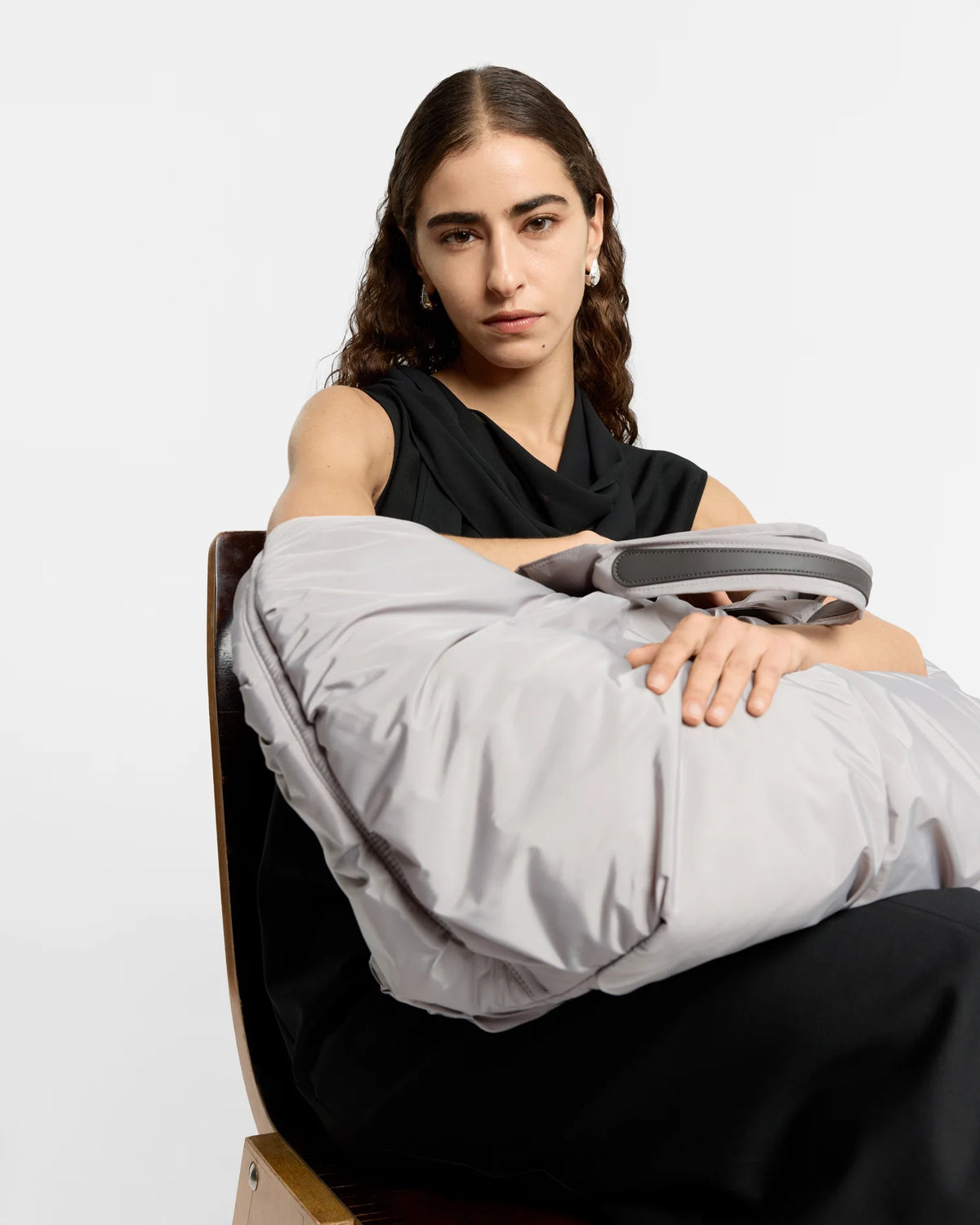 Woman sitting carrying the Caba Weekender Tote Bag in Dove by Vee Collective, wearing a minimalistic outfit against a clean studio background.