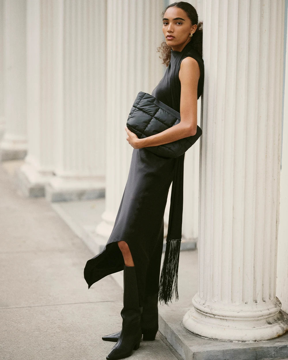 On-body shot of a woman with the Porter Basque Clutch in Matt Black, leaning on a white column.