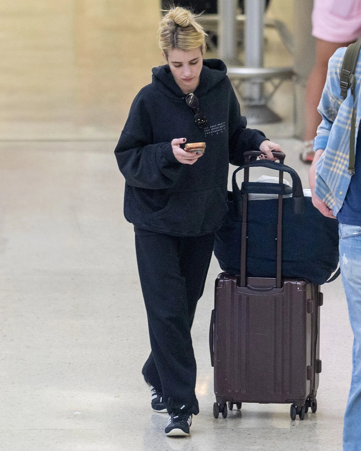 A picture featuring a model wearing a black hoodie and pants, walking in an airport with a Midnight Essence Trench Weekender bag and luggage.
