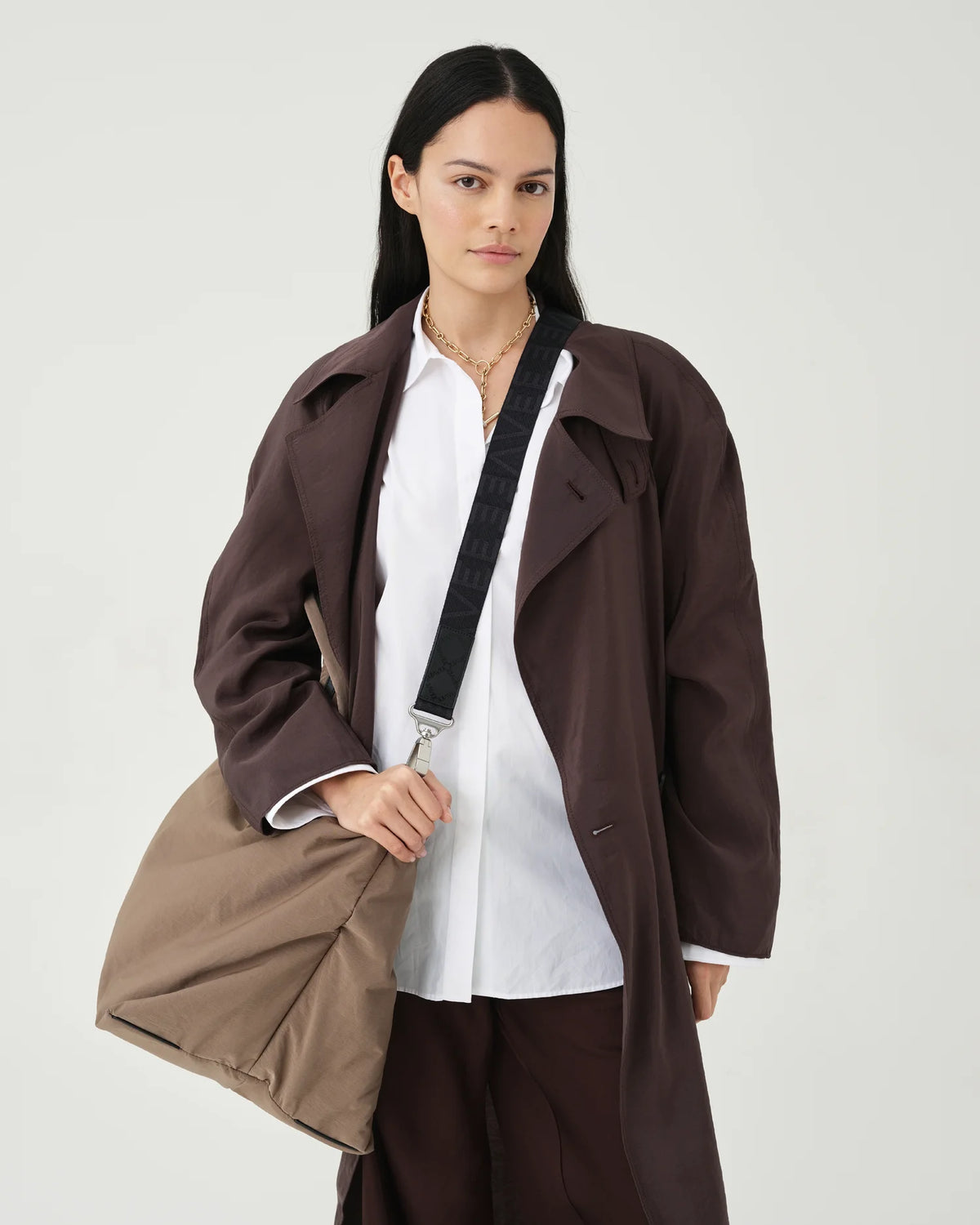 A photo of a person wearing a brown coat and holding a mink Essence Tote Bag against a white background.