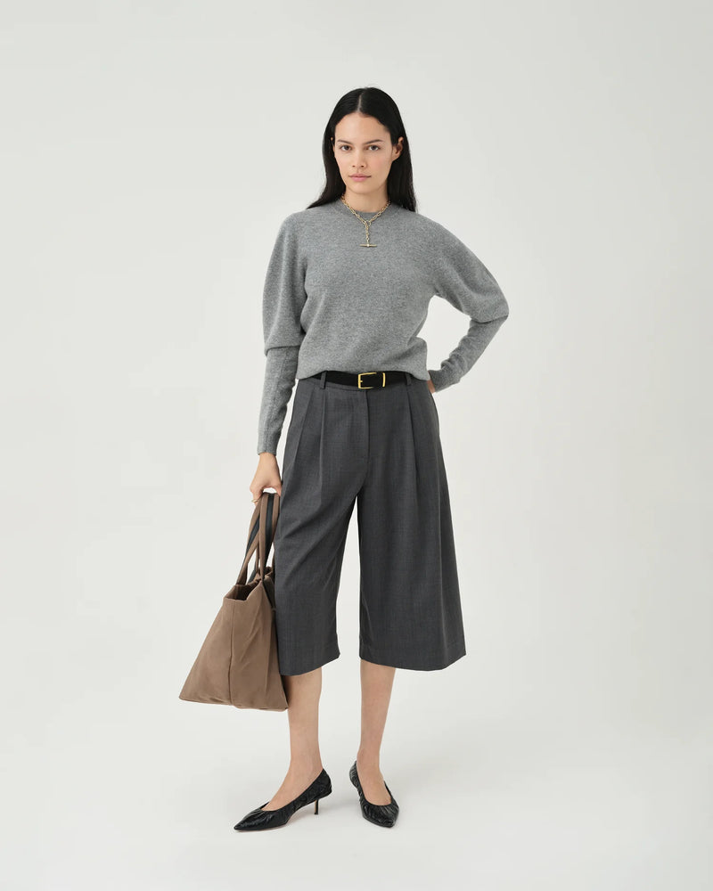 A photo of a model wearing a gray sweater and dark pants, holding a mink Essence Tote Bag against a white background.