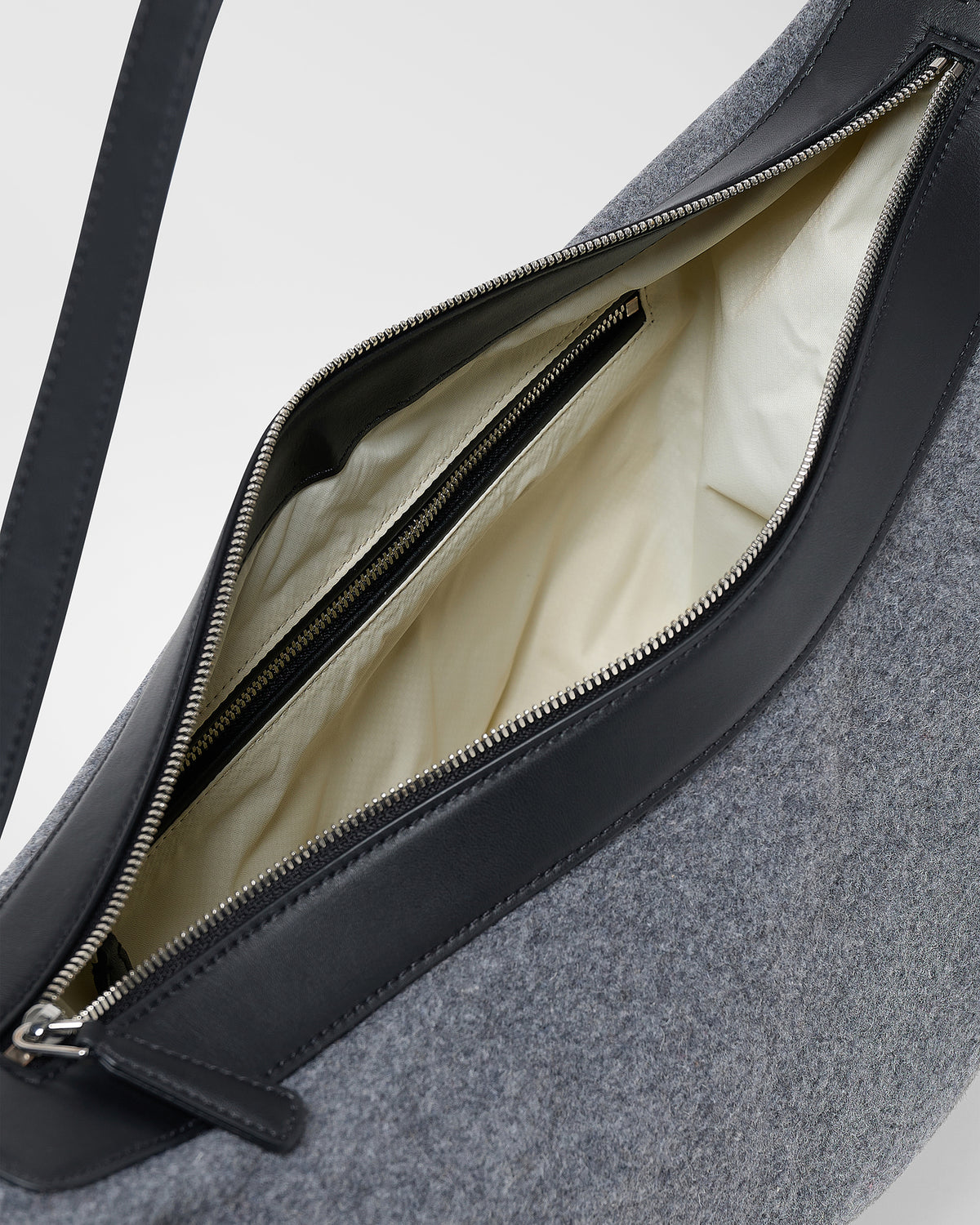 A close-up product photo of an open charcoal Essence Wool Banana bag, showcasing its cream coloured interior lining, black straps, and silver zipper hardware.