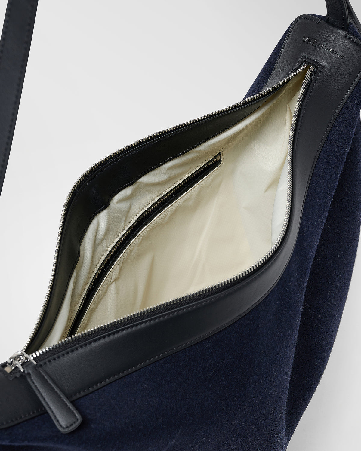 A close-up product photo of an open Essence Wool Banana bag, showcasing its cream-coloured interior lining, black straps, and silver zipper hardware.